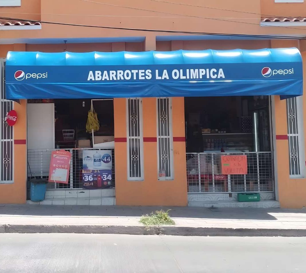 Toldos de lona tapasol azul con letras blancas 'Abarrotes La Olímpica' sobre entrada de tienda de abarrotes