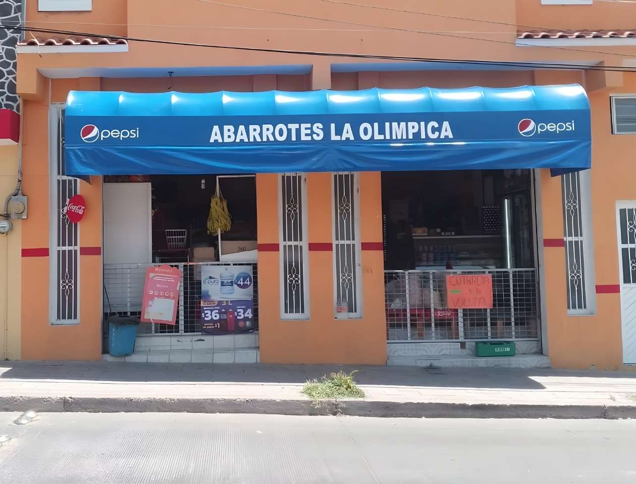 Toldos de lona tapasol azul con letras blancas 'Abarrotes La Olímpica' sobre entrada de tienda de abarrotes