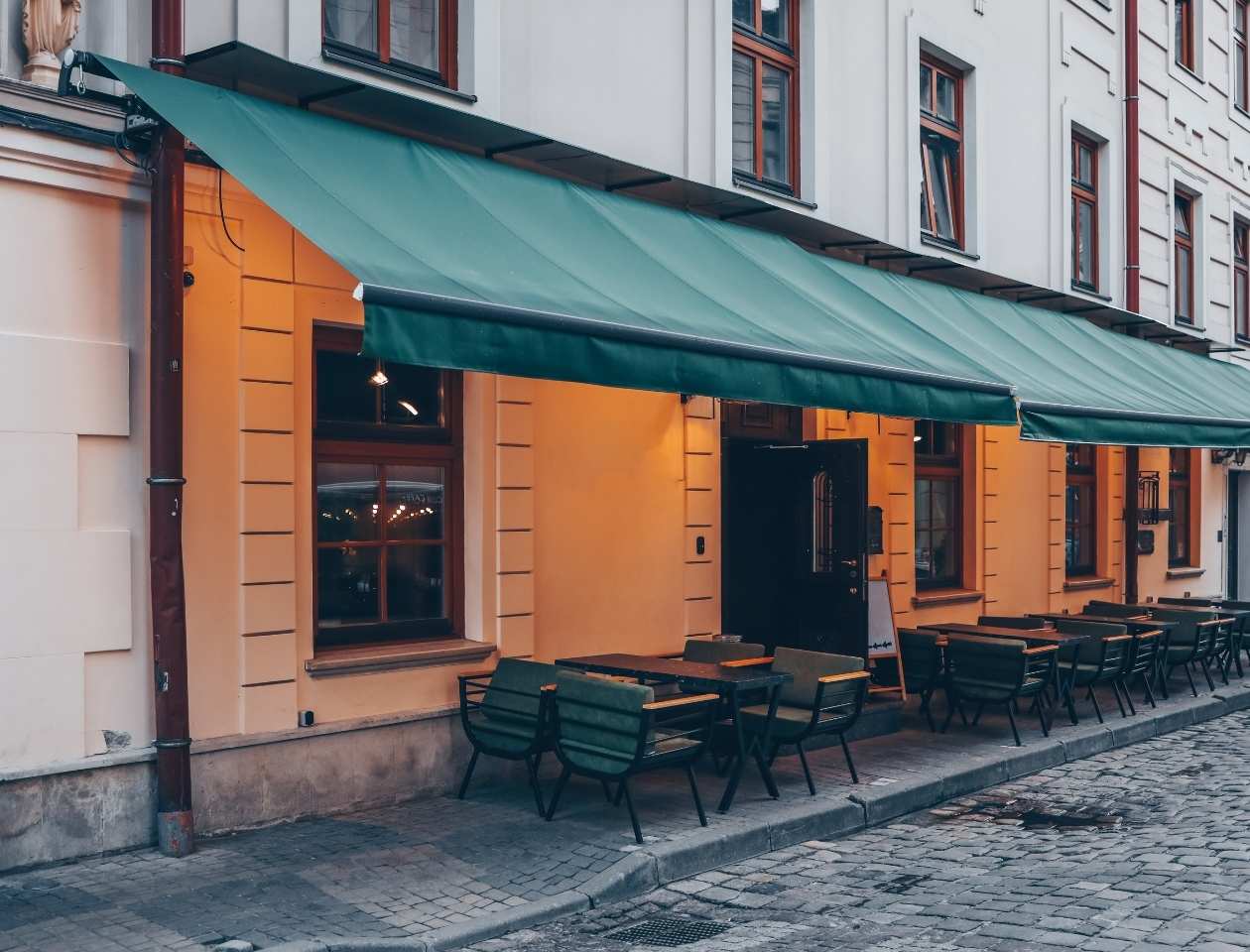 Toldos de lona tapasol verde instalado sobre ventanas de restaurante con mesas en terraza exterior