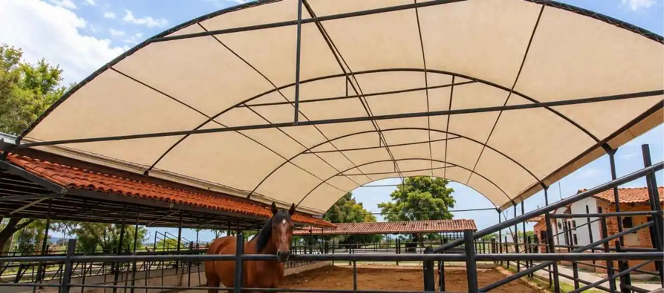 Techado de malla sombra beige en estructura metálica para área ecuestre y corral de caballos.
